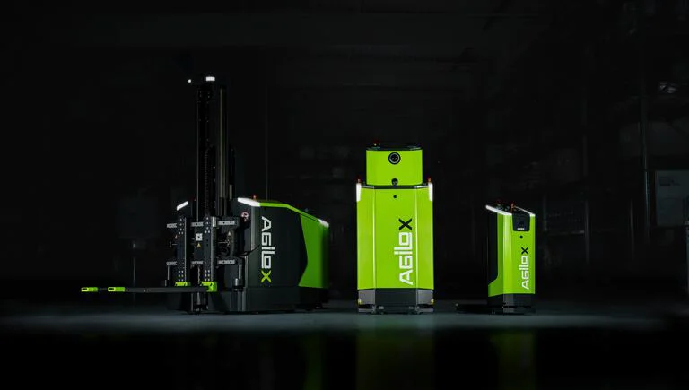  Das Bild zeigt eine Flotte von automatisierten, fahrerlosen Transportrobotern in verschiedenen Größen, mit einem hervorgehobenen grünen Roboter der Marke "Agilox".